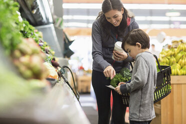 Mutter und Sohn sehen sich die Einkaufsliste an, während sie im Supermarkt an den Regalen stehen - CAVF33198