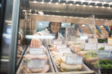 Female worker arranging food in display cabinet at supermarket - CAVF33206