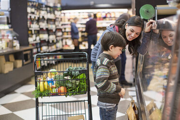 Lächelnde Frau sieht ihren Sohn an, der an einer Vitrine im Supermarkt steht - CAVF33214