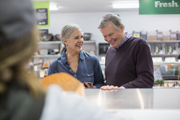 Smiling couple standing by counter at supermarket - CAVF33215