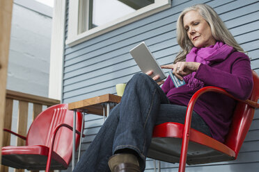 Niedriger Blickwinkel einer Frau beim Online-Shopping, während sie auf einem Stuhl auf der Veranda sitzt - CAVF33226