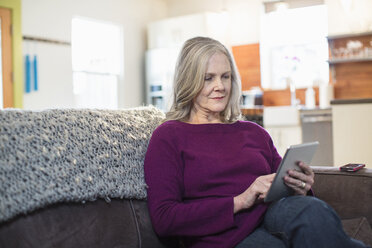 Senior woman using tablet computer while sitting on sofa at home - CAVF33227