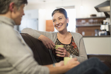 Smiling female friends talking while sitting on sofa at home - CAVF33230