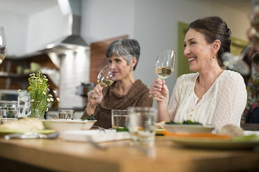 Lächelnde Freundinnen trinken Wein, während sie bei einem geselligen Beisammensein am Tisch sitzen - CAVF33238