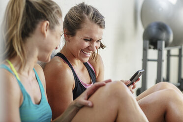 Glückliche Freundinnen benutzen ein Mobiltelefon im Fitnessstudio - CAVF33261