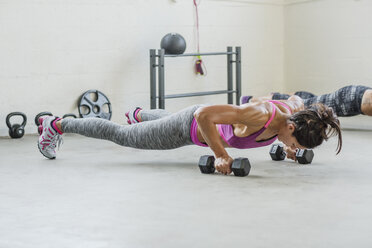 Female athletes holding dumbbells and doing push-ups in gym - CAVF33275