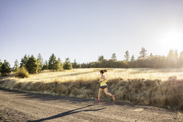 Full length of woman jogging on field against clear sky during sunny day - CAVF33312