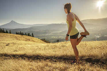 Seitenansicht einer Frau, die auf einem grasbewachsenen Berg gegen den Himmel an einem sonnigen Tag trainiert - CAVF33316