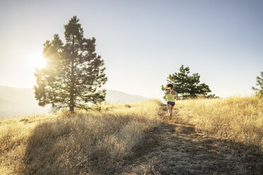 Rear view of woman jogging on mountain against clear sky during sunny day - CAVF33322