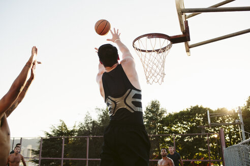 Mann spielt Basketball mit Freunden im Hof gegen den klaren Himmel - CAVF33370