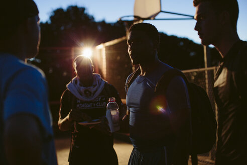 Freunde diskutieren in der Abenddämmerung auf dem Basketballplatz - CAVF33374