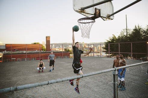 Freunde beobachten einen Mann, der beim Basketballtraining im Hof eintaucht - CAVF33375