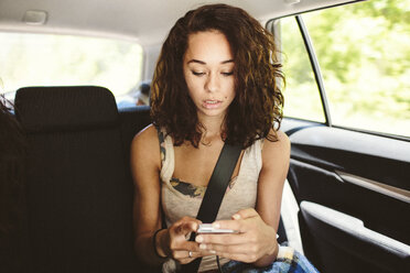 Woman using mobile phone while traveling in car - CAVF33446