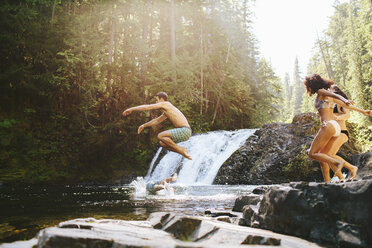 Cheerful friends jumping into river in forest - CAVF33465