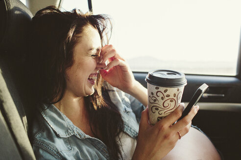 Happy woman with coffee cup using mobile phone while traveling in car - CAVF33476