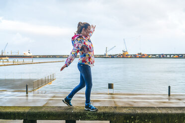 Azores, Sao Miguel, Woman walking on top of stone bench in Ponta Delgada harbor - KIJF01912