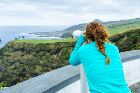 Azoren, Sao Miguel, Frau schaut durch ein Touristenfernglas auf das Meer, lizenzfreies Stockfoto