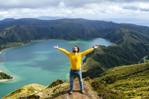 Azoren, Sao Miguel, Mann mit erhobenen Armen und geschlossenen Augen auf dem Gipfel der Lagoa do Fogo, lizenzfreies Stockfoto