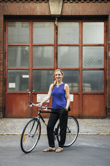 Frau steht mit Fahrrad in der Stadt - FOLF06683