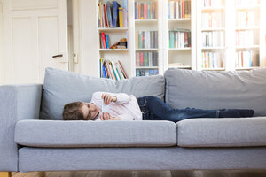 Girl lying on couch at home holding cell phone - LVF06848