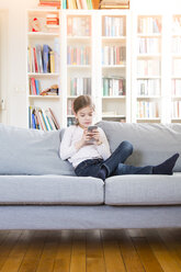 Girl sitting on couch at home holding cell phone - LVF06849