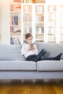 Mädchen sitzt zu Hause auf der Couch und hält ein Mobiltelefon in der Hand - LVF06849