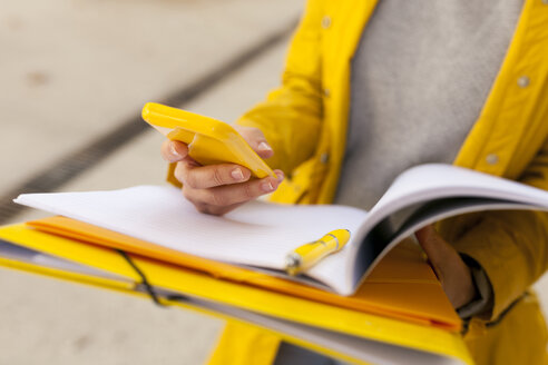 Close-up of woman with cell phone and folder outdoors - VABF01533