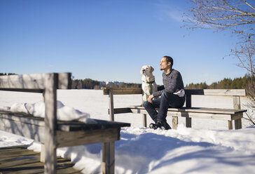 Mann sitzt mit Hund auf einer Bank im Winter - FOLF06845