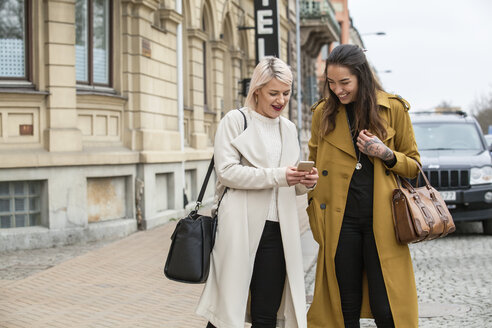 Zwei Frauen schauen auf der Straße auf ihr Smartphone - FOLF06862