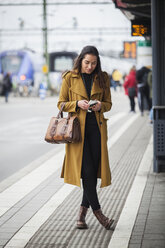 Junge Frau schaut am Bahnhof auf ihr Smartphone - FOLF06866