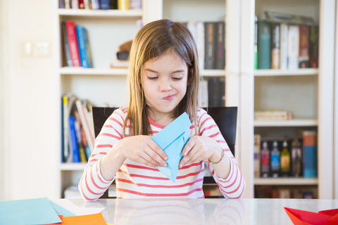 Girl tinkering with paper on table at home stock photo