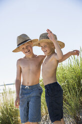 Shirtless boys in straw hats standing on dune at seashore - FOLF06979