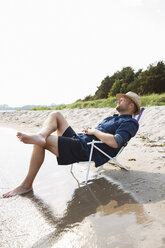 Älterer Mann sitzt auf einem Liegestuhl am Meer - FOLF06982