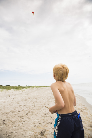 Hemdloser Junge mit Drachen am Strand, lizenzfreies Stockfoto