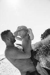 Shirtless man holding boy in straw hat at beach - FOLF06988