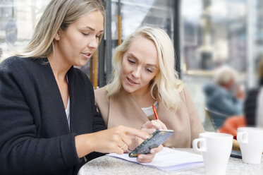 Junge Frauen benutzen ein Mobiltelefon in einem Straßencafé - FOLF07077