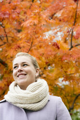 Young woman wearing overcoat against autumn tree - FOLF07117