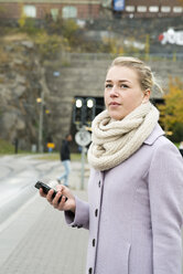 Nachdenkliche junge Frau auf der Straße mit Smartphone in der Hand - FOLF07121