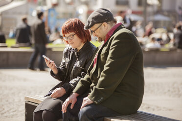 Woman with down syndrome sitting on bench and checking smart phone together with boyfriend - FOLF07229