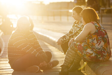 Frau mit Down-Syndrom sitzt mit Freunden bei Sonnenuntergang auf der Promenade - FOLF07237