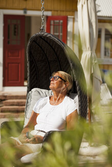 Ältere Frau sitzt in einem Strandkorb mit Kapuze und hört Musik auf ihrem Smartphone - FOLF07255
