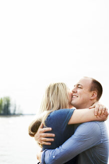 Lächelndes, sich umarmendes Paar mit See im Hintergrund - FOLF07360