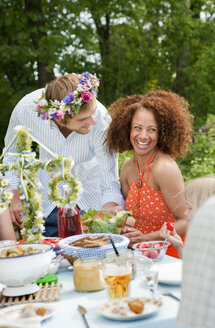 Mann mit Blumenkranz im Gespräch mit einem Mädchen, das am Picknicktisch sitzt - FOLF07473