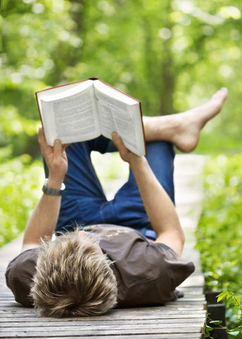 Young man lying down on wooden jetty and reading book stock photo