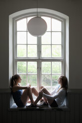 Zwei Mädchen im Teenageralter sitzen auf der Fensterbank - FOLF07500
