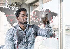 Casual businessman touching glass pane with world map in office - UUF13183