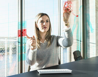 Junge Geschäftsfrau berührt eine Projektionsfläche mit Daten im Büro - UUF13194