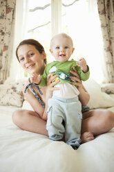 Teenage girl sitting in bed holding little sister - FOLF07627