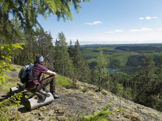 Hiker sitting on wooden bench in forest and looking at view - FOLF07643
