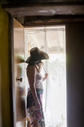Frau mit Sonnenhut schaut durch einen Türvorhang - FOLF07655